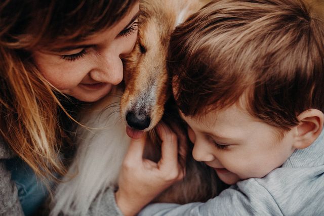 Crop cheerful mom with boy caressing and embracing purebred dog with tongue out while spending time together